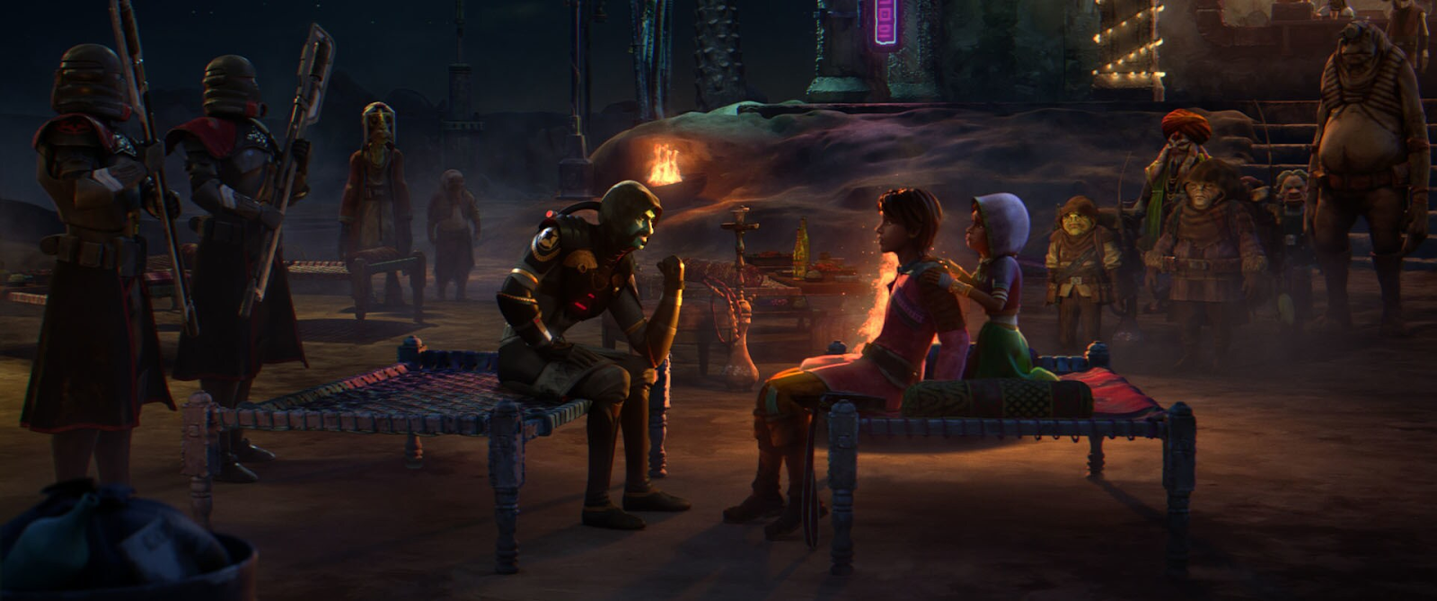 Four people are in a room; one is seated wearing a VR headset, while the others stand nearby observing a computer screen.